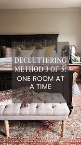 Home "Bedroom with a dark wooden bed frame, patterned pillows, and a tufted bench at the foot of the bed. Text overlay reads: 'Decluttering Method 3 of 5: One Room at a Time'."